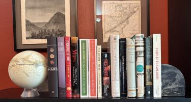 Rectangular photo of David Baron’s office bookshelf showing works on Mars, Percival Lowell, and Camille Flammarion (the first person to describe “canals” on Mars), along with a historical photo of people watching an eclipse and a map showing an eclipse path of totality. Photo credit: David Baron.