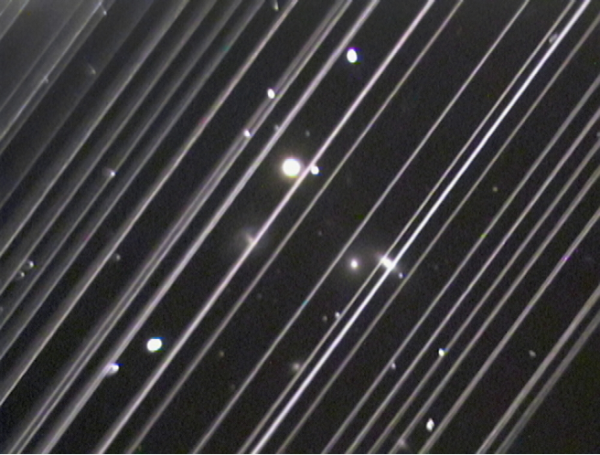 A black and white image of the dark night sky with white streaks spanning across the image from the top right to bottom left, and white spots throughout the background.