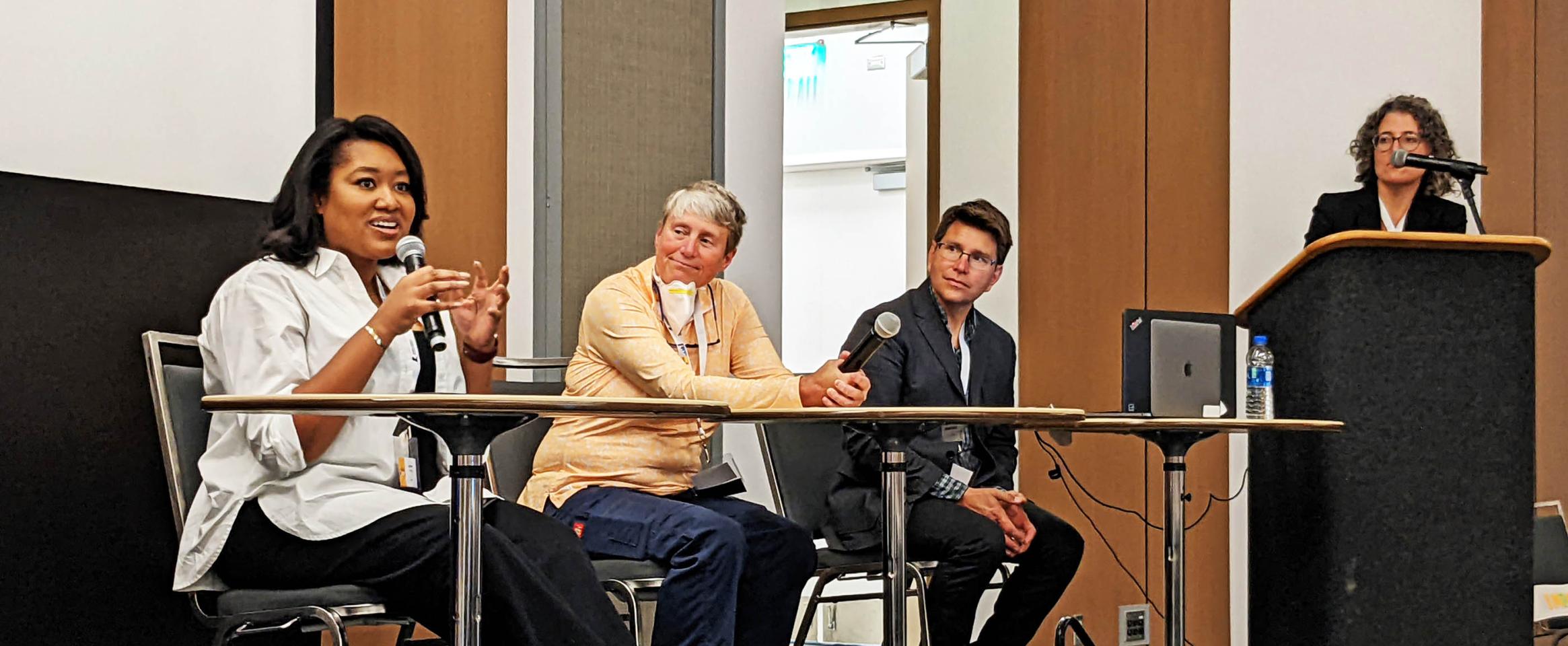 Horizontal photo of Zakiya Whatley speaking, seated along side Ginger Campbell and Stephen Ornes, with Sarah Webb at podium, during the Pump up Your Podcast session. Photo by Laura Castañón