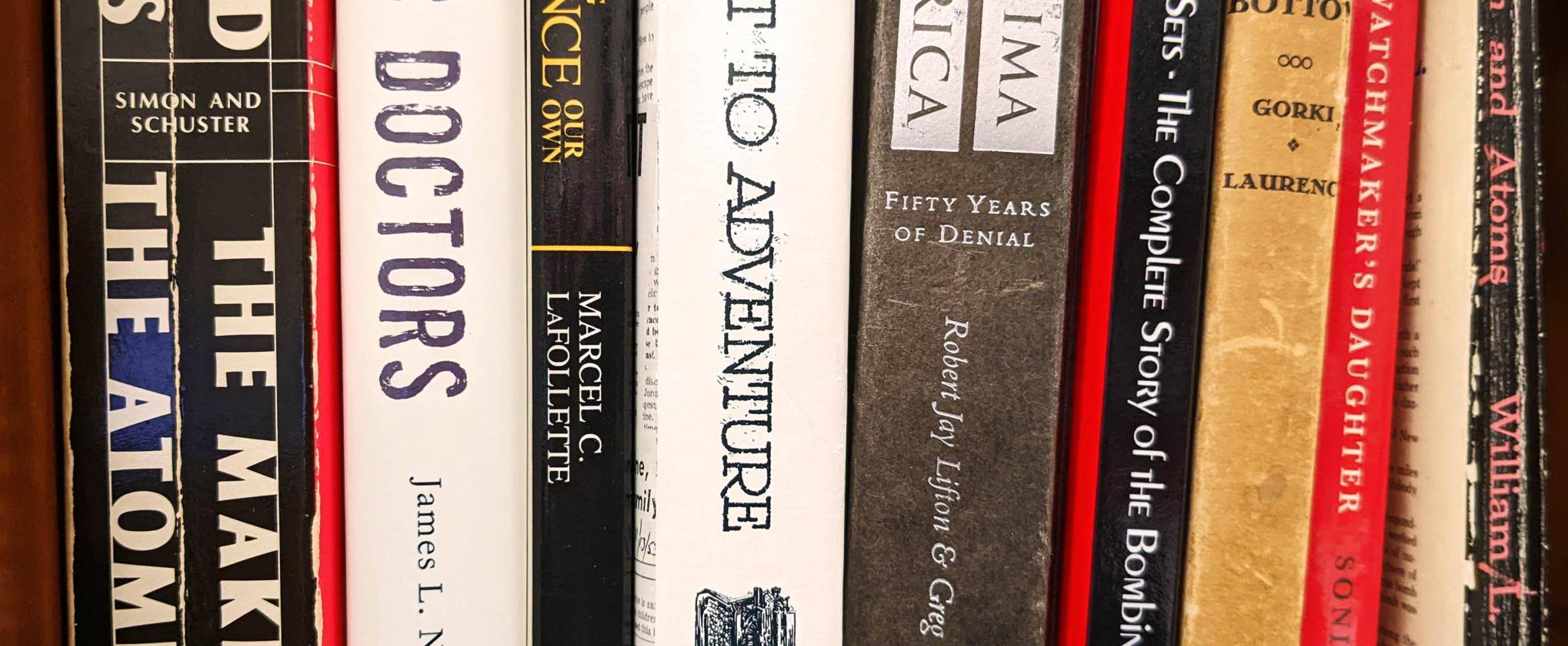 Rectangular photo of a close up view of books on a bookshelf, with spines facing out and many titles related to atomic science and history.