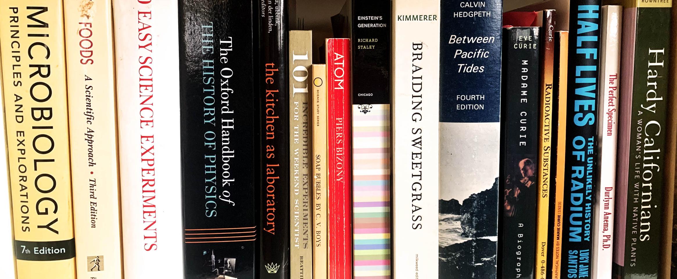 Rectangular photo of a closeup of books on a shelf, spanning titles on science, California, and microbiology. Photo by Liz Lee Heinecke