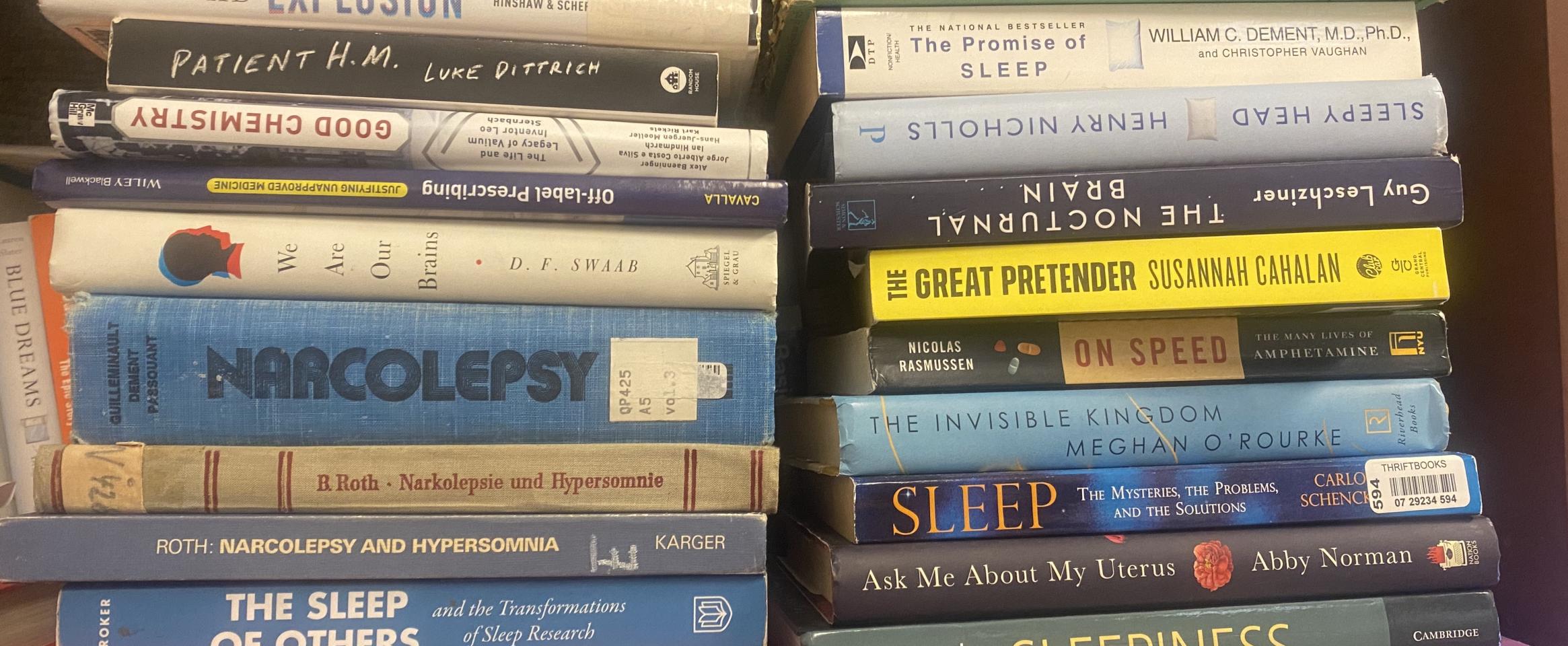 Rectangular photo of Quinn Eastman’s office bookshelf showing books on narcolepsy, sleep science, and the medical care system. Photo credit Quinn Eastman.