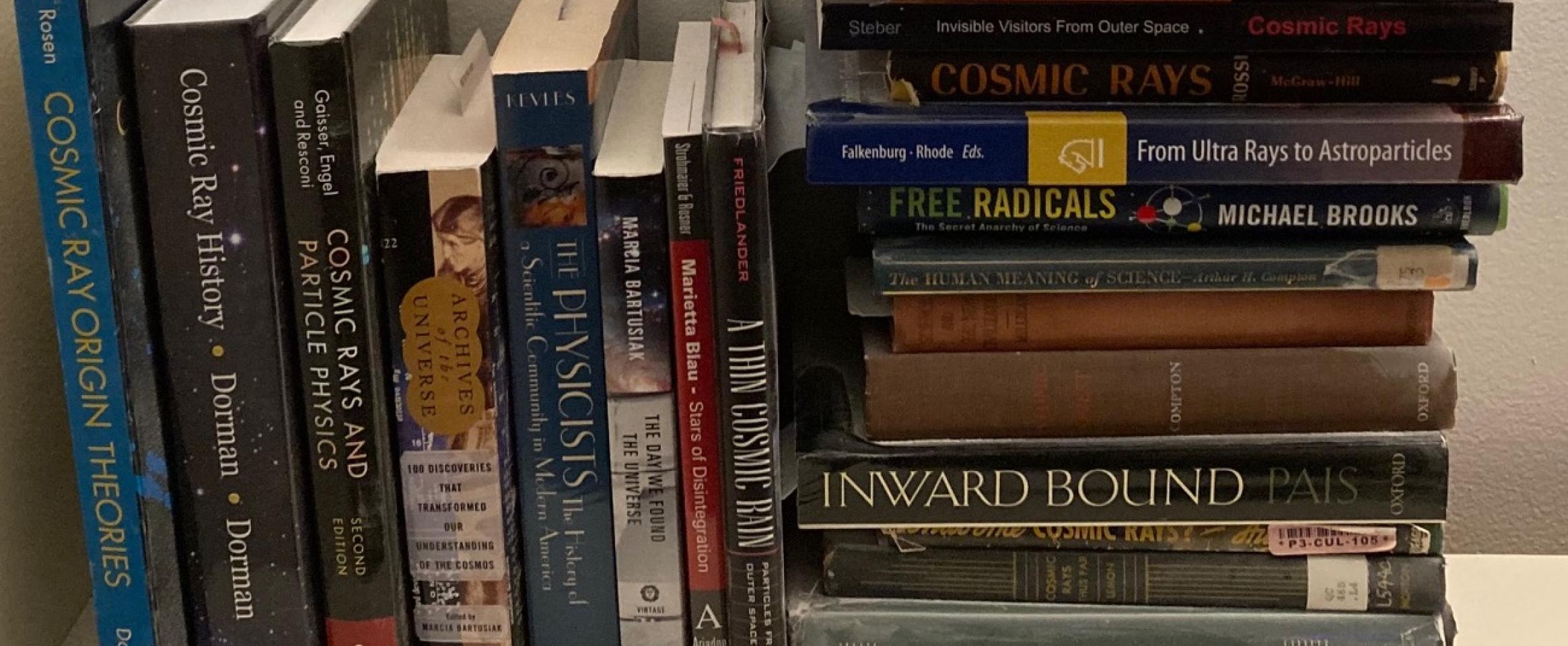 Rectangular photo of Mark Wolverton’s office bookshelf showing works by and about physicists Arthur Holly Compton and Robert Millikan, the subjects of his book Splinters of Infinity, along with books on cosmic rays, stars, astronomy, and physics. Photo credit: Mark Wolverton.