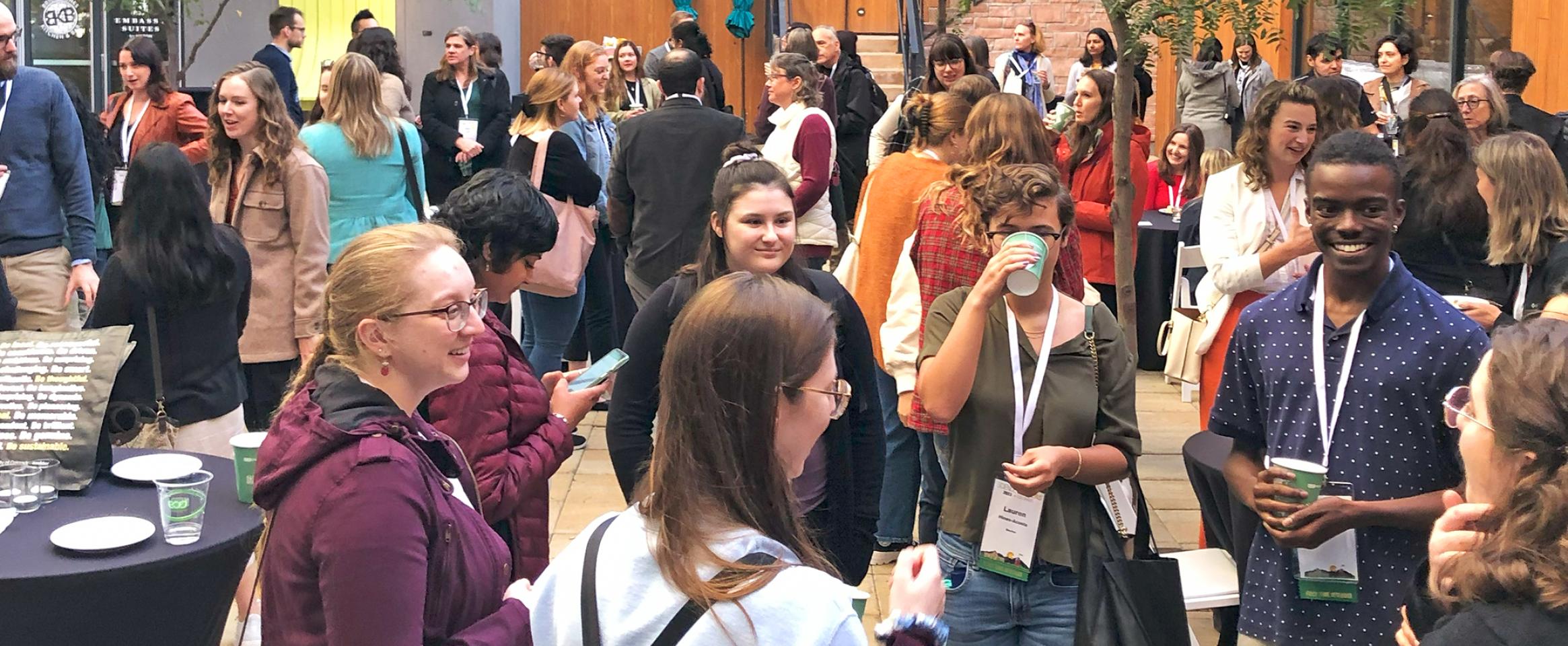 Vertical photo of attendees mingling in a hotel outdoor courtyard, with name badge ribbons visible. Photo by Ben Young Landis