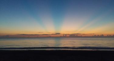 Photo of a colorful sunrise over the horizon of a calm ocean offshore of Melbourne, Florida. The morning light is barely peeking, blending into the night.