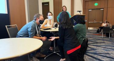 Some attendees lean into the stage to ask the panelists questions during the Interviewing for Narrative Science Stories session at Science Writers 2022, with moderator Katharine Gammon looking on from the background.