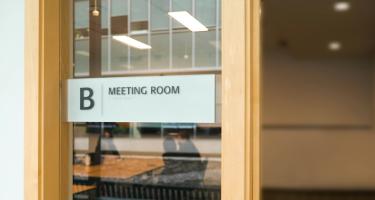Closeup of room number sign outside office meeting room. Photo by <a href="https://unsplash.com/@2hmedia?utm_source=unsplash&utm_medium=referral&utm_content=creditCopyText">2H Media</a> on <a href="https://unsplash.com/photos/a-sign-on-a-glass-door-that-says-meeting-room-ZIMJQWbg41Q?utm_source=unsplash&utm_medium=referral&utm_content=creditCopyText">Unsplash</a>
