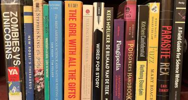 Rectangular photo of Mindy Weisberger’s office bookshelf showing works on zombies, poisons, fungi, parasites, nature writing, and non-fiction writing. Photo credit: Mindy Weisberger.