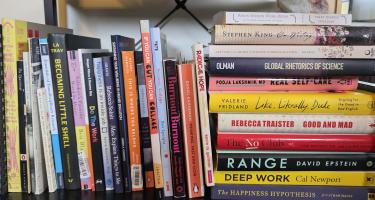 Rectangular photo of Bethann Garramon Merkle’s office bookshelf showing an eclectic mix of books on science communication, writing, poetry, collage art, feminism, burnout, and happiness. Photo credit: Bethann Garramon Merkle