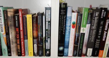 Rectangular photo of Dennis Meredith’s office bookshelf showing works on climate change, climate change and society, climate justice, dire predictions, extinctions, and the war on science. Photo credit: Dennis Meredith.