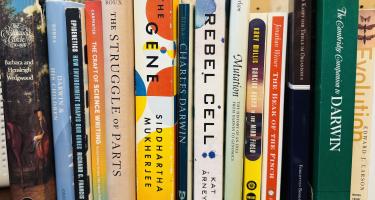 Rectangular photo of Roxanne Khamsis office bookshelf showing several books by and about Charles Darwin, along with books on genes, evolution, how environment shapes genes, cells, and mutations. Photo credit: Roxanne Khamsi. 