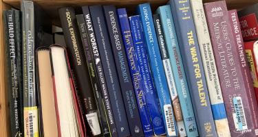 Rectangular photo of Helen Pearson’s office bookshelf showing works on such topics as evidence-based medicine, using evidence, evidence-based management, principles of medical statistics, testing treatments, users’ guides to the medical literature, and how to read a paper. Photo credit: Helen Pearson 