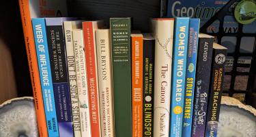Rectangular photo of Lisa M. Pinsker Munoz’s office bookshelf showing books about and by women in science and challenges they faced in progressing in their careers. Photo credit Lisa M. Pinsker Munoz.