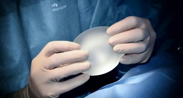 Close-up of a plastic surgeon's gloved hands holding a new breast implant.
