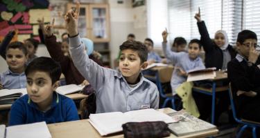 Alt text: Children in a classroom with their hands raised to answer a question.
