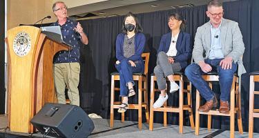Horizontal photo of Peter Aldhous speaking at the podium next to seated panelists Lisa Song, who is masked, Stephanie Lee, and Nicholas Florko. Photo by Gabriella Lewis.
