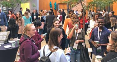 Vertical photo of attendees mingling in a hotel outdoor courtyard, with name badge ribbons visible. Photo by Ben Young Landis