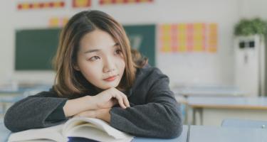 Photo of girl in classroom looking away from the camera with an open book on her desk.