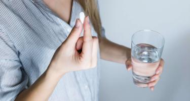 Close-up of a woman holding a pill and a glass of water, ready to take medication.