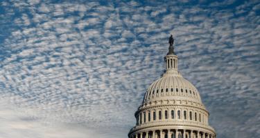 The top half of the Capitol building, with an American flag in front of it blowing in the wind.