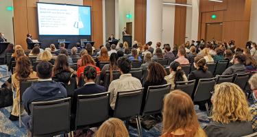 Horizontal photo of the Preprints session at Sci Wri 22 shot from back of the room, showing rows of seats filled with attendees. Panelists are seated on the stage, and the screen slide reads Some journalists doubt preprints are here to say. Photo credit David Jen.