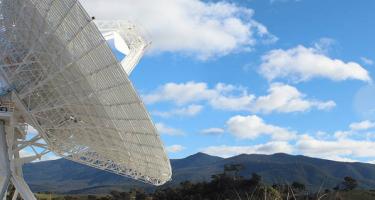 Photo of Deep Space Station 36, a gigantic antenna dish situated against rolling Australian hills and clear sky with clouds.