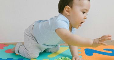 A baby boy in a blue shirt playing on a puzzle mat.