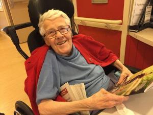 Photo of Joan Hollobon smiling and looking up from magazines and mail. Photo courtesy of S W C C