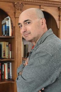 Vertical photo of Elliot Richman posing in front of an ornate bookcase. Photo courtesy of Elliot Richman and University of Rochester