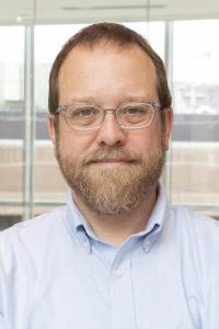 Portrait photo of Tom Ulrich wearing a beard and glasses inside an office building
