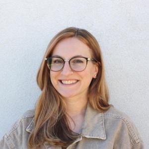 Leighana Luther: Woman with glasses smiling against a white wall backdrop.