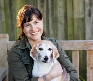 Portrait photo of Melanie Kaplan and her beagle, Hammy on a bench in an outdoor setting.