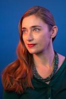 Vertical headshot photo of Alisson Clark, with long hair and looking off camera, with a studio backdrop