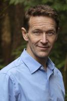 Vertical headshot photo of Alisson Clark, with short hair and a collared dress shirt, against a wooded backdrop