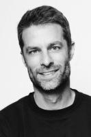 Vertical headshot photo of Kai Kupferschmidt with short hair, light beard, and crew-neck shirt in studio backdrop