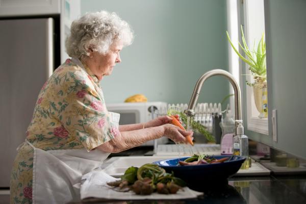 Older woman washing vegetables under running water at a sink